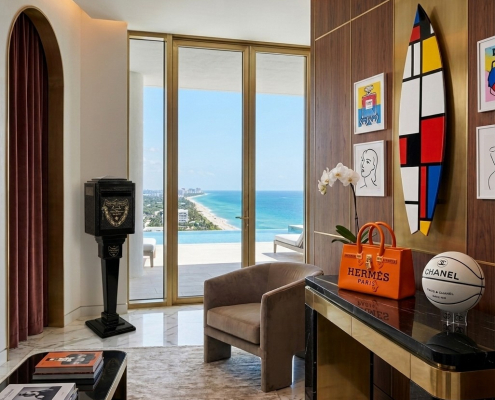 Luxury Palm Beach penthouse living room featuring Hermès Birkin sculpture, Chanel basketball, and Mondrian surfboard art with ocean view.